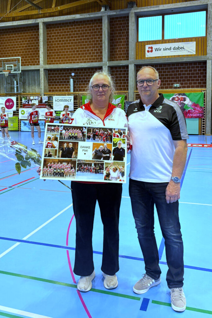 Two adults stand in a gym holding a large photo collage thanking Pia, smiling at the camera.