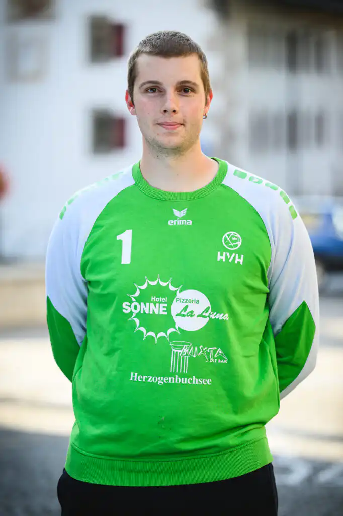 Portrait of a young man in a bright green jersey with white sleeves and the number 1, standing outdoors. Sponsor logos are visible on the shirt.