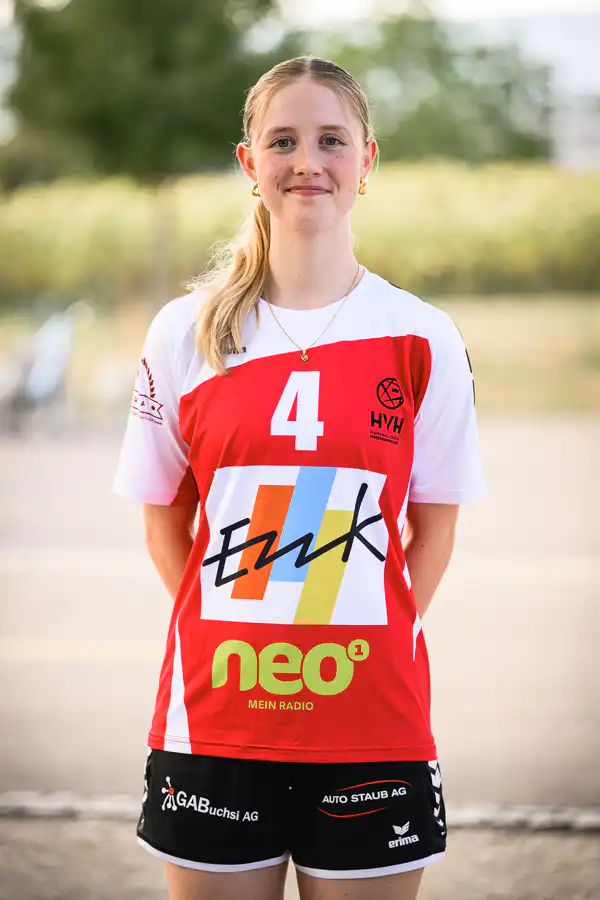 Young woman athlete standing outdoors in a red-and-white sports jersey with the number 4, smiling at the camera.