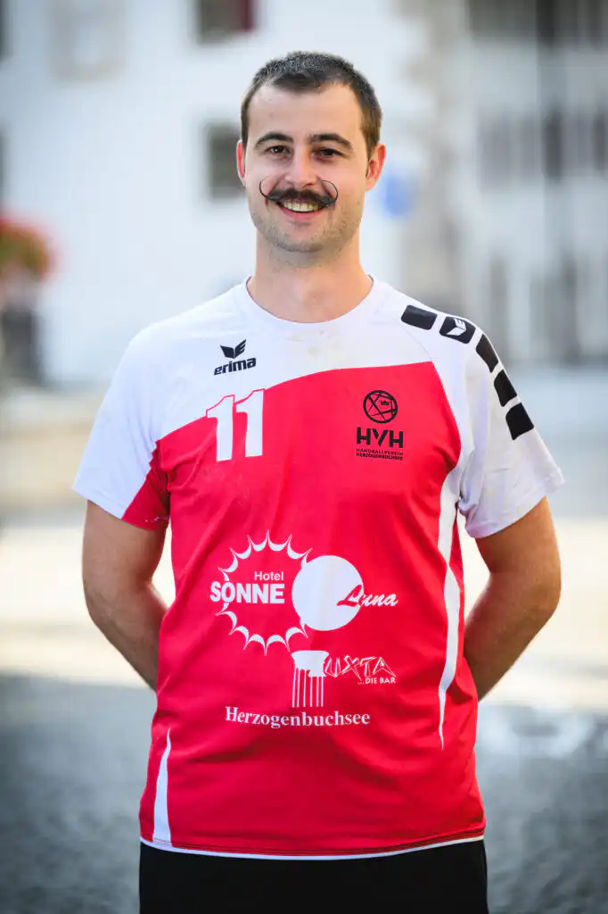 Smiling man in a red and white sports jersey with number 11, standing outdoors.