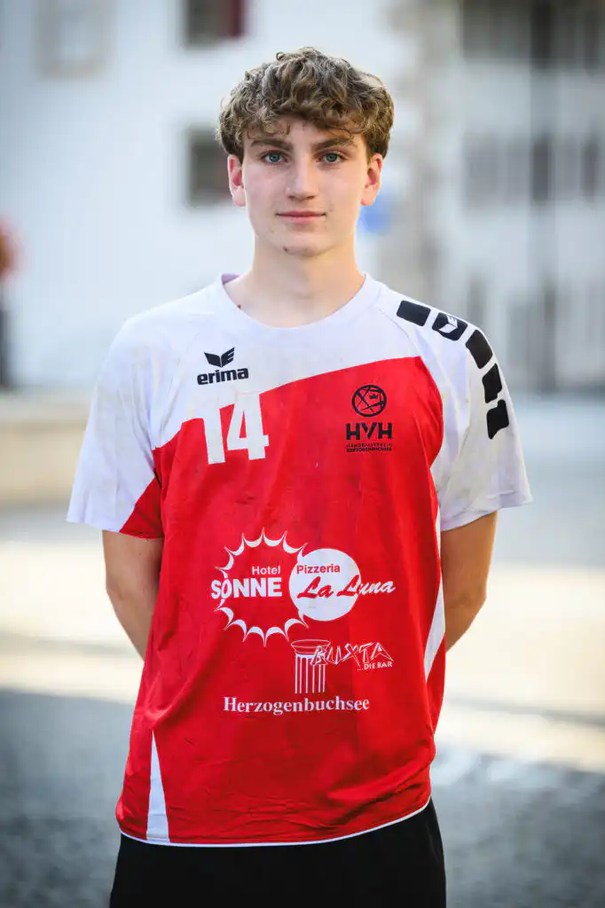 Young male athlete wearing a white and red handball jersey with number 14, standing outdoors.