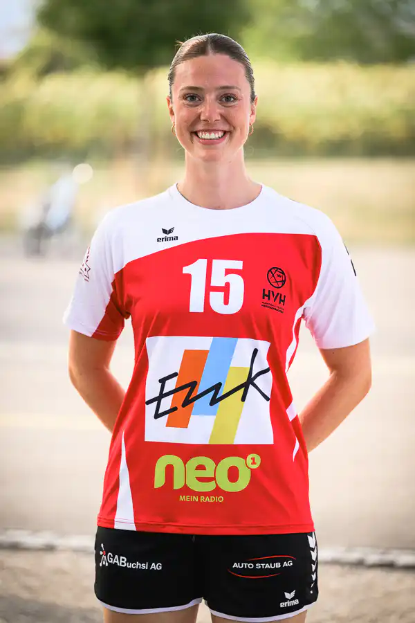 Smiling female athlete in a red-and-white jersey with number 15, standing outdoors.