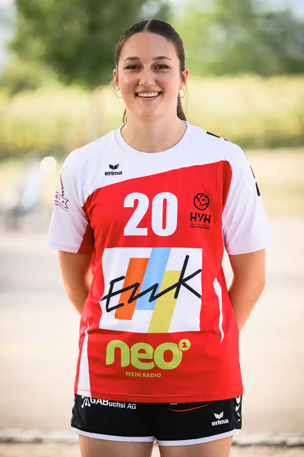 Smiling female athlete standing outdoors in a red-and-white jersey with the number 20 and sponsor logos.