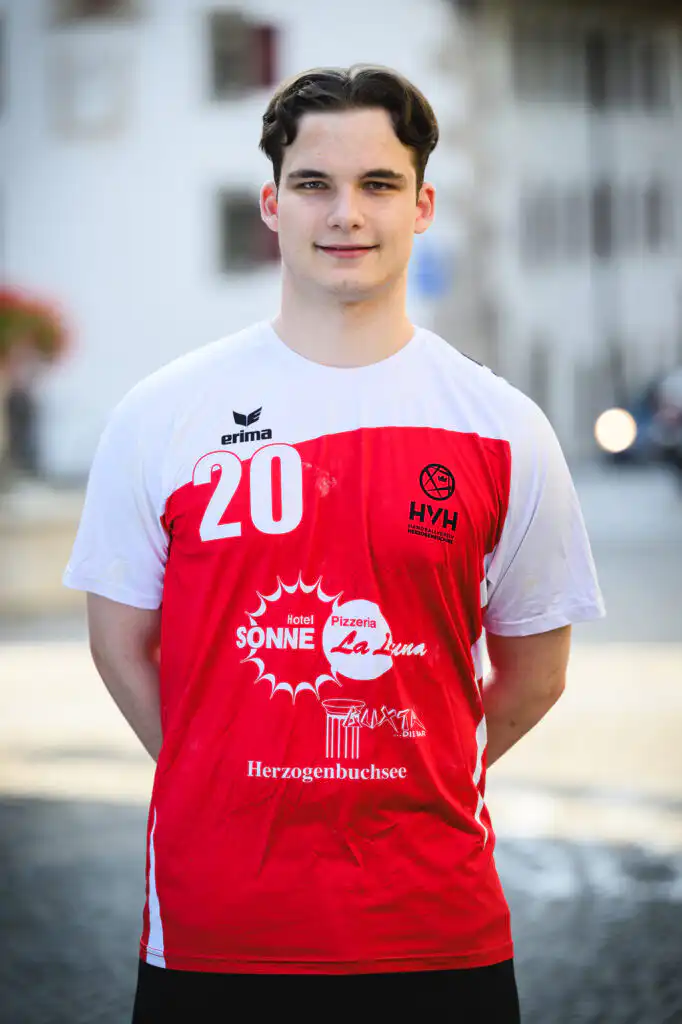 Young man in a white and red sports jersey with number 20, standing outdoors.