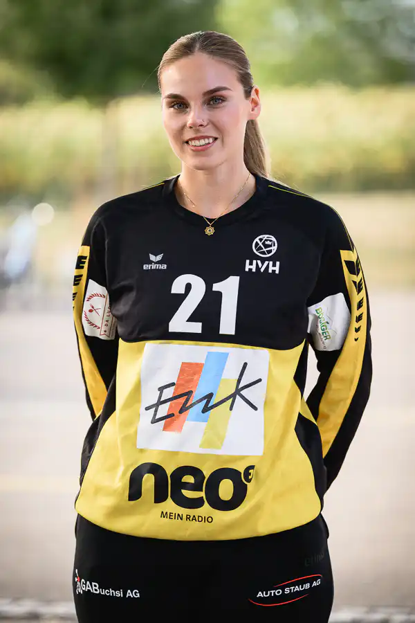 Young woman athlete in a black and yellow sports jersey with the number 21, smiling outdoors.