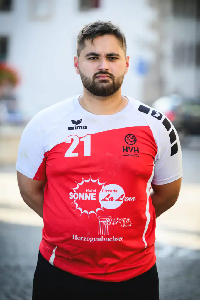 Portrait of a man with a beard wearing a white and red sports jersey with the number 21, standing outdoors.