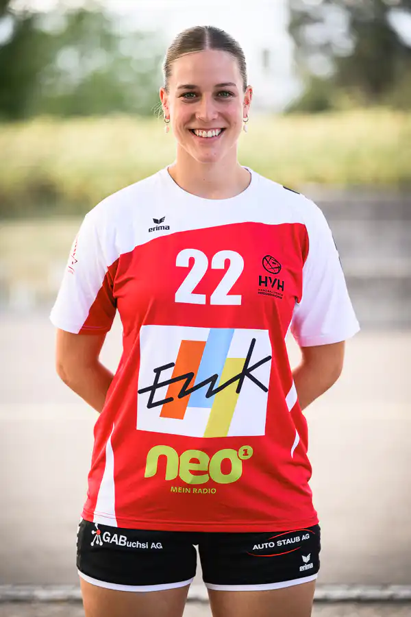 Smiling female athlete wearing a red-and-white sports jersey with the number 22 and sponsor logos on the chest and shorts.