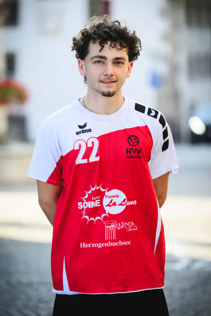 Young man with curly hair in a red-and-white sports jersey, number 22, standing outdoors.
