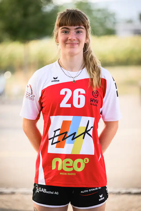 Female athlete wearing a red-and-white jersey with the number 26, standing outdoors and smiling.