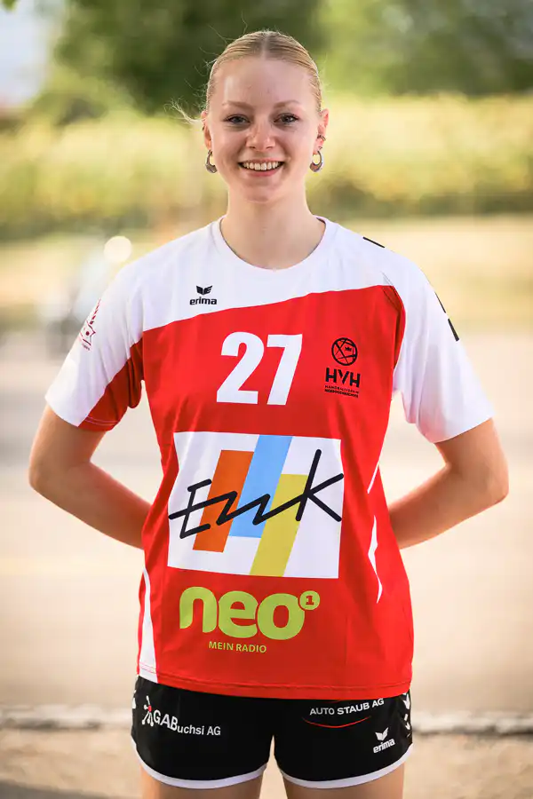 Smiling female athlete in a red-and-white jersey with number 21, standing outdoors with hands on hips.